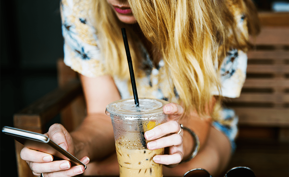 Frau mit Handy und Kaffee-To-Go-Becher